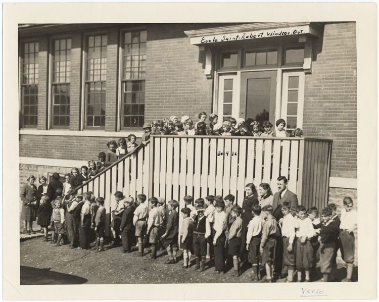 Reproduction d’une photographie de l’ouverture de la nouvelle &eacute;cole bilingue Saint-Robert, rue Wyandotte-Ouest, Windsor (Ontario), le 30 septembre 1936, l’inspecteur Robert Gauthier et les enseignantes, Mabel Parent et Fernande St-Pierre, accueillant les &eacute;l&egrave;ves, 1936.