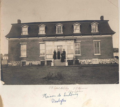 Reproduction d’une photographie du p&egrave;re Guillaume Lebel, le fr&egrave;re G. Roy et les p&egrave;res Louis H&eacute;roux et Eug&egrave;ne Lefebvre devant le presbyt&egrave;re de la paroisse Sainte-Anne-de-Sudbury (Ontario), ca 1910.
